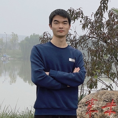 一名年轻的亚洲男性,从腰部以上展示。他留着深色头发,穿着一件深蓝色的长袖衬衫。在他身后是一个雾蒙蒙的湖泊和一些树木。